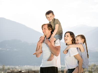 Una famiglia felice con due bambini si gode la vista sulle montagne – i genitori portano i bambini sulle spalle.