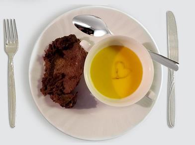 Plate with pumpkin soup in a cup and a slice of roast; a heart shape decorates the soup’s surface.