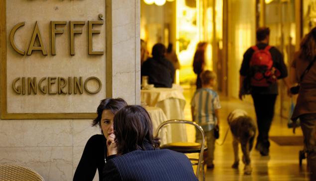 Menschen im Gespräch vor dem Caffè Gingerino in Bozen, im Hintergrund Passanten unter den Lauben.