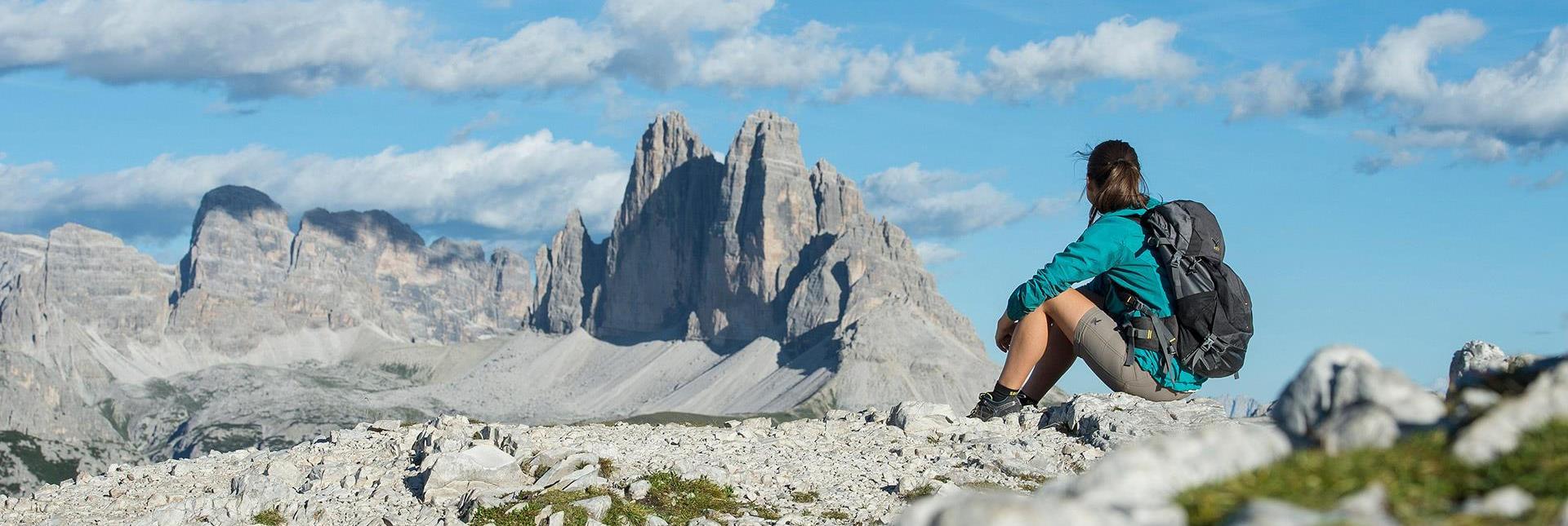Eine Wanderin sitzt auf einem Felsen mit Blick auf die Drei Zinnen